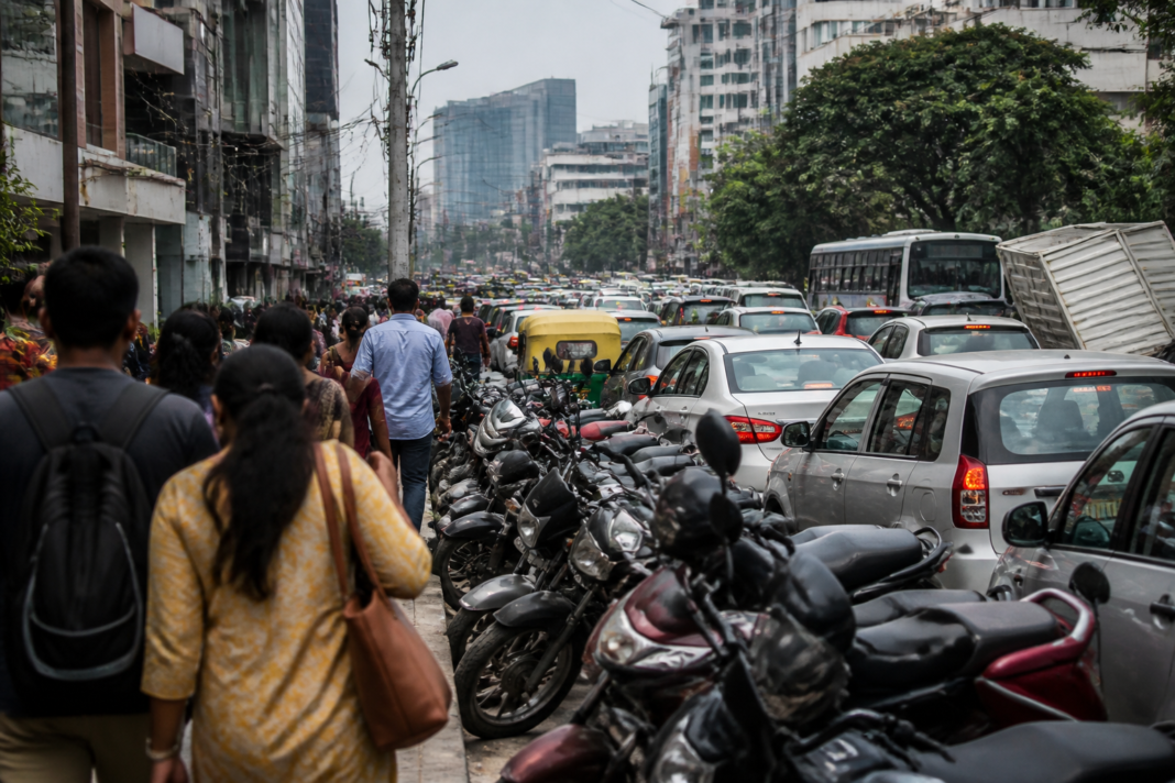 Roadside vehicles parked along a busy Bengaluru street amid traffic and urban buildings