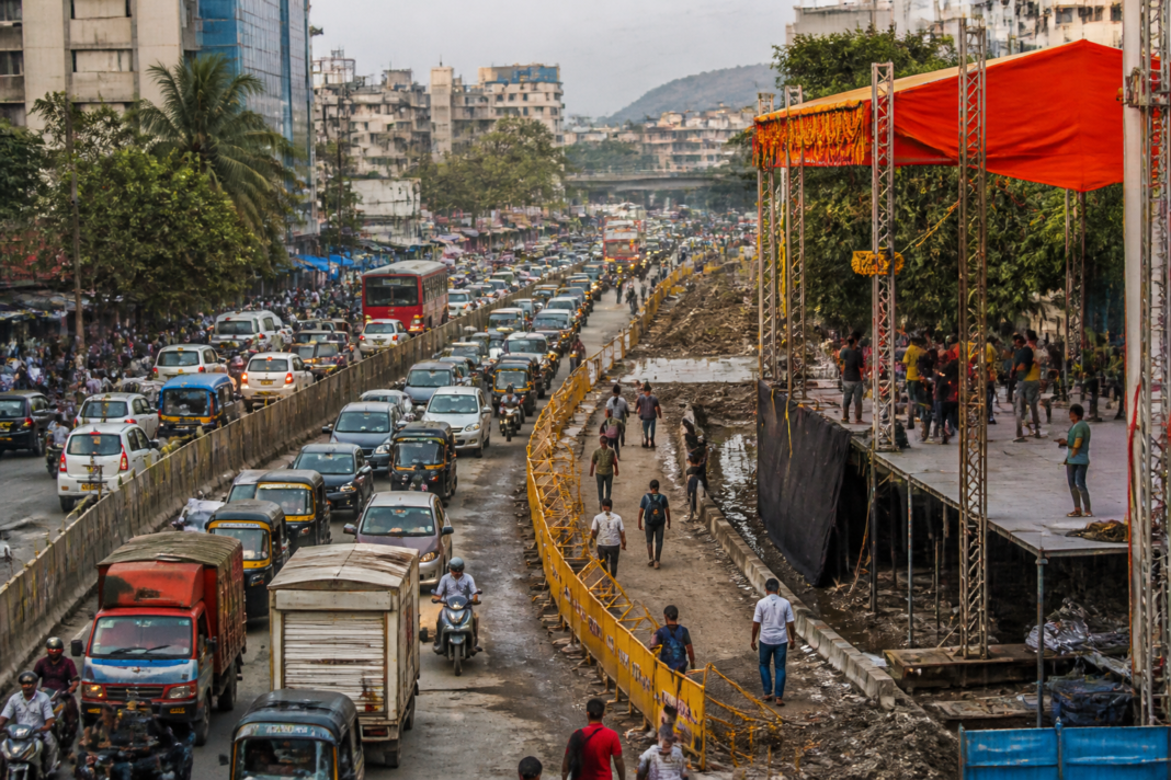 Traffic moving past a Dahi Handi celebration stage on a crowded road in Ambernath