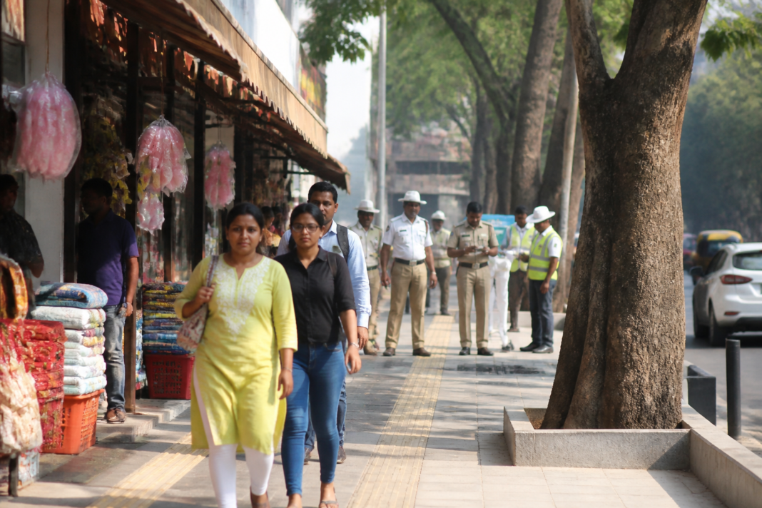 Pedestrians walking along a Bengaluru footpath beside roadside commercial activity