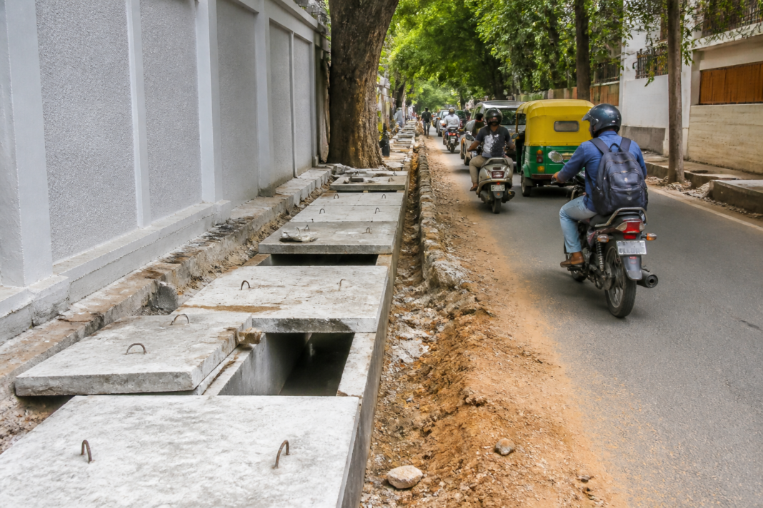 Roadside drain works and concrete covers along a congested residential street in Cooke Town, Bengaluru