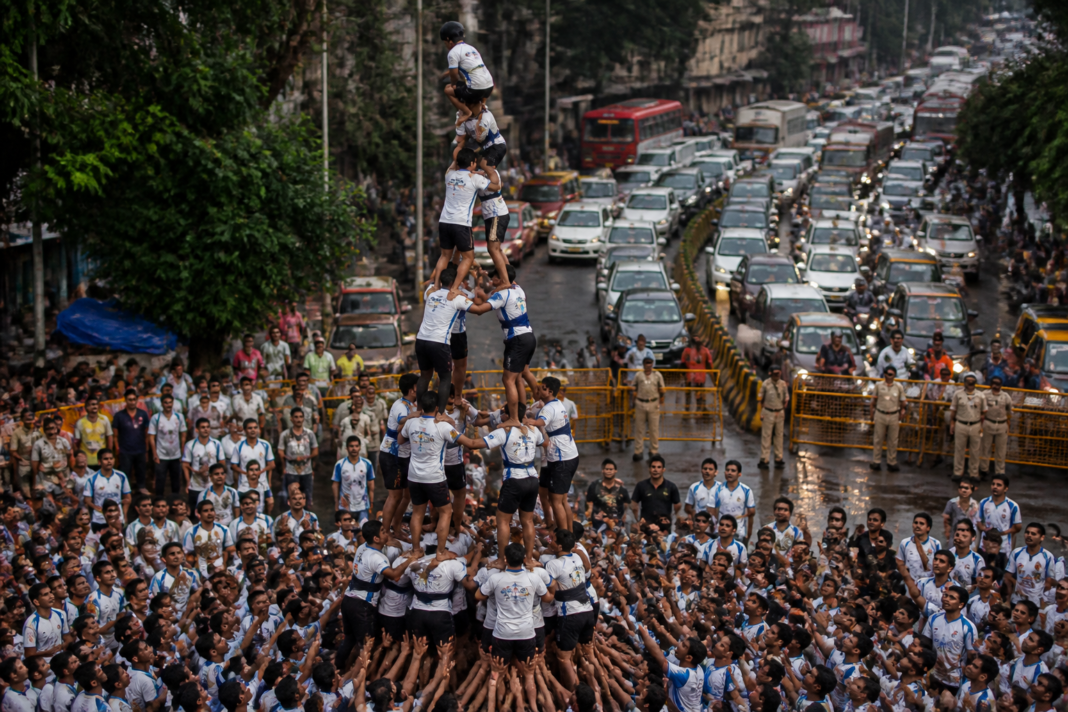Govinda participants forming a human pyramid during a Dahi Handi event on a crowded Thane road