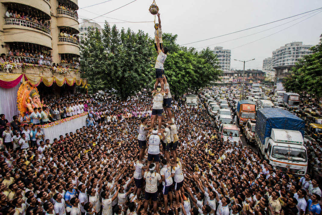Govinda participants forming a human pyramid during a Dahi Handi celebration on a crowded Vasai-Virar road