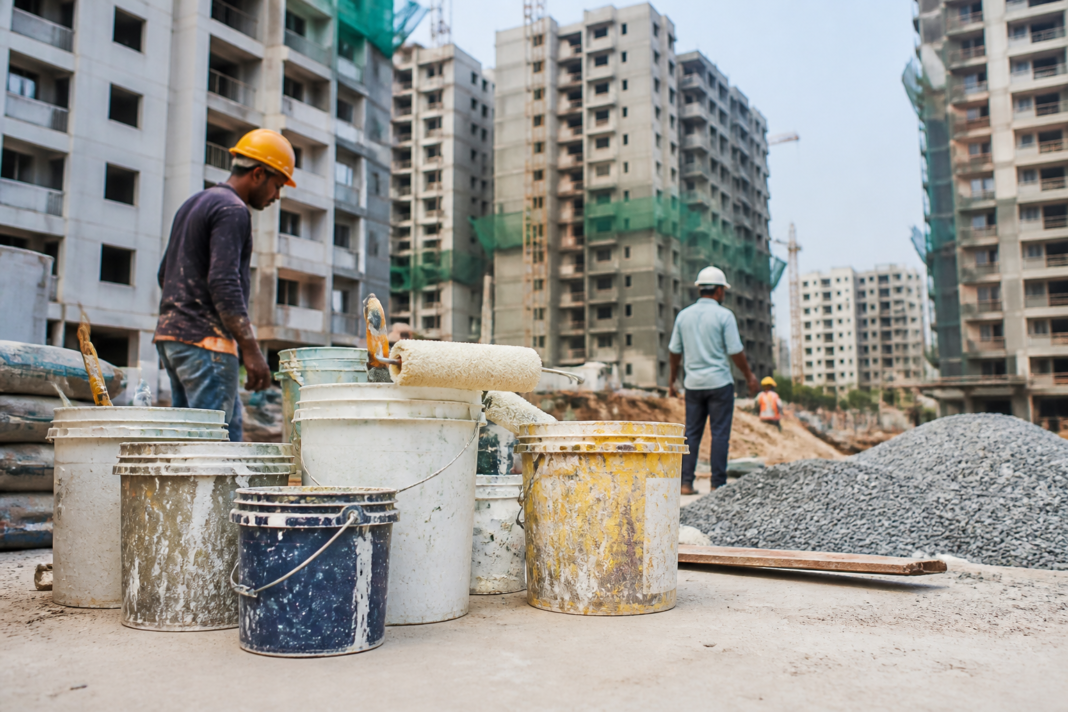 Paint containers and construction materials arranged at an urban building site, illustrating the Indian paint industry and demand from housing and infrastructure.