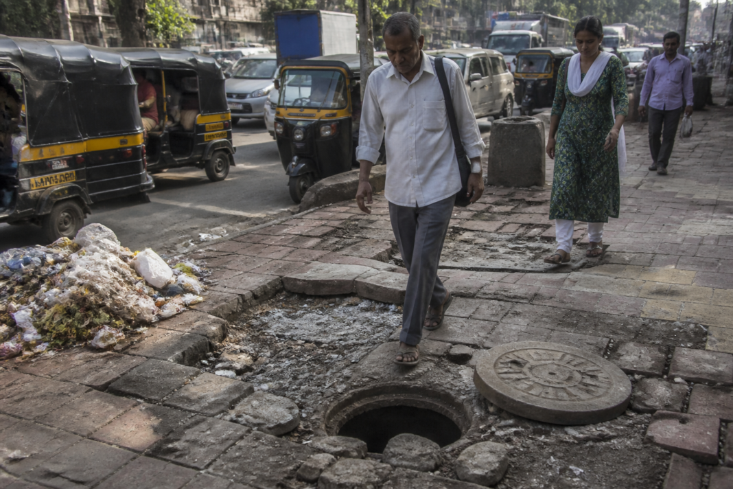 Damaged pavement and roadside garbage on a Mumbai street, illustrating the city’s civic maintenance problems