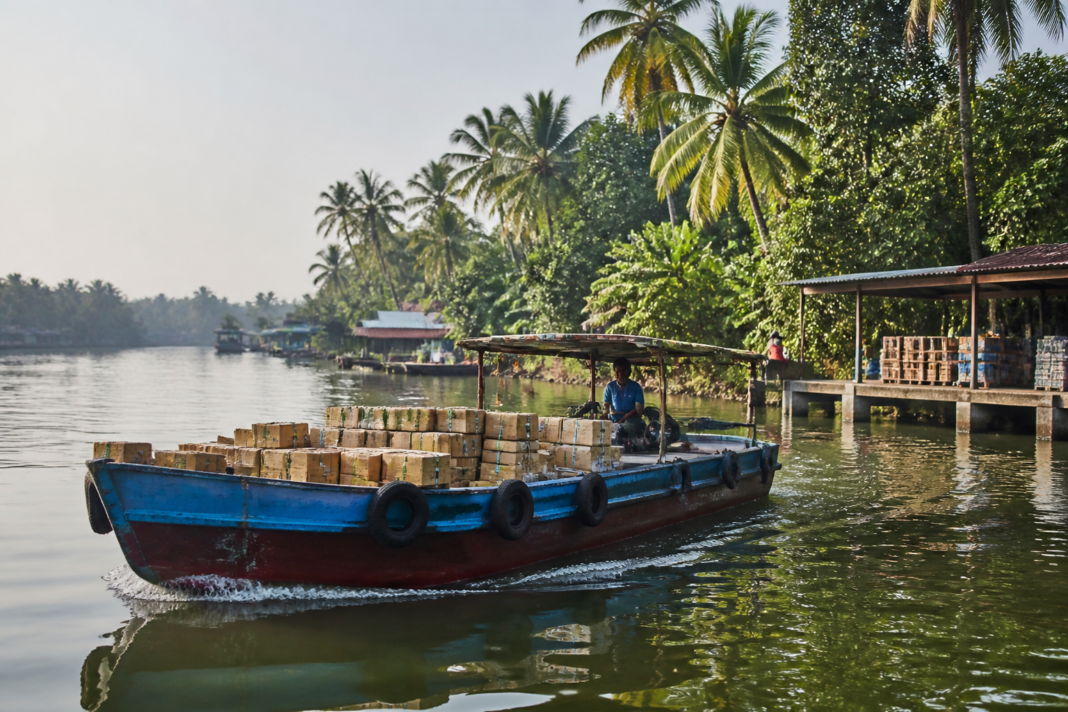 Boat carrying cargo along an inland waterway near settlements in Kerala as part of India’s last-mile logistics network