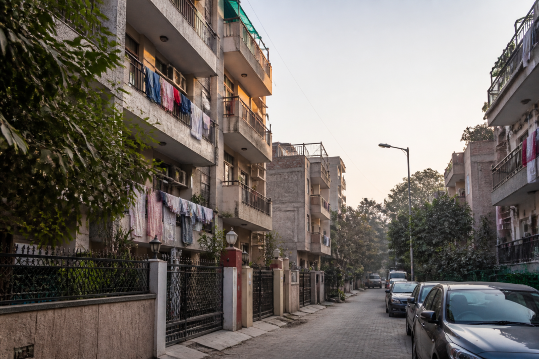 A dense Delhi residential building used for student PG accommodation, showing closely packed balconies and narrow urban streets