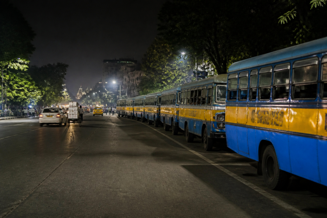 City buses parked in a single row along a designated Kolkata roadside area at night