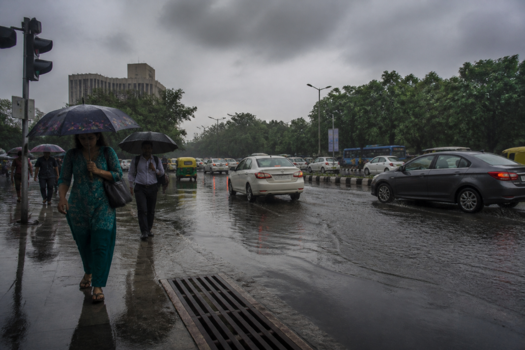 Delhi weather forecast showing rain clouds over a waterlogged urban road