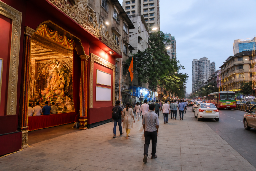 Mumbai Ganpati advertisements displayed near a festival mandal entrance beside a city footpath