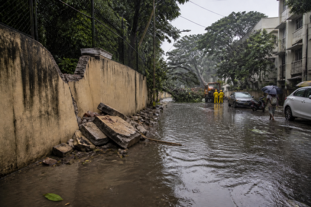 Bengaluru rain flooding a city road near fallen trees and damaged compound walls
