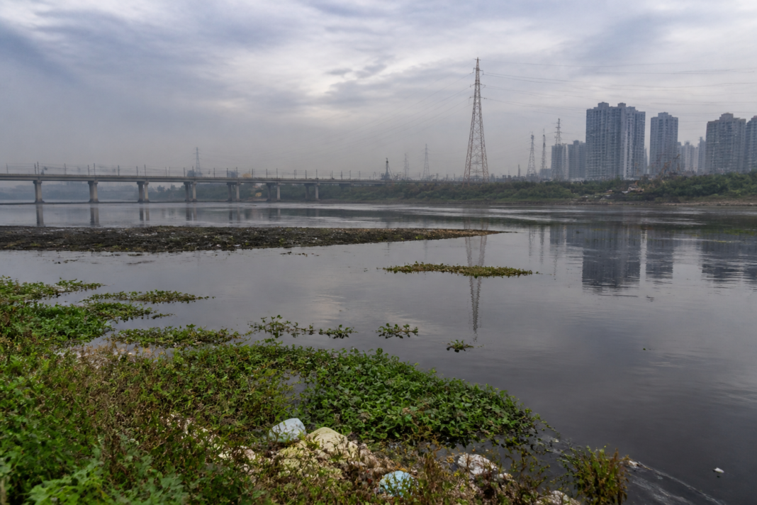 Yamuna river in Delhi with urban buildings and polluted water under an overcast sky