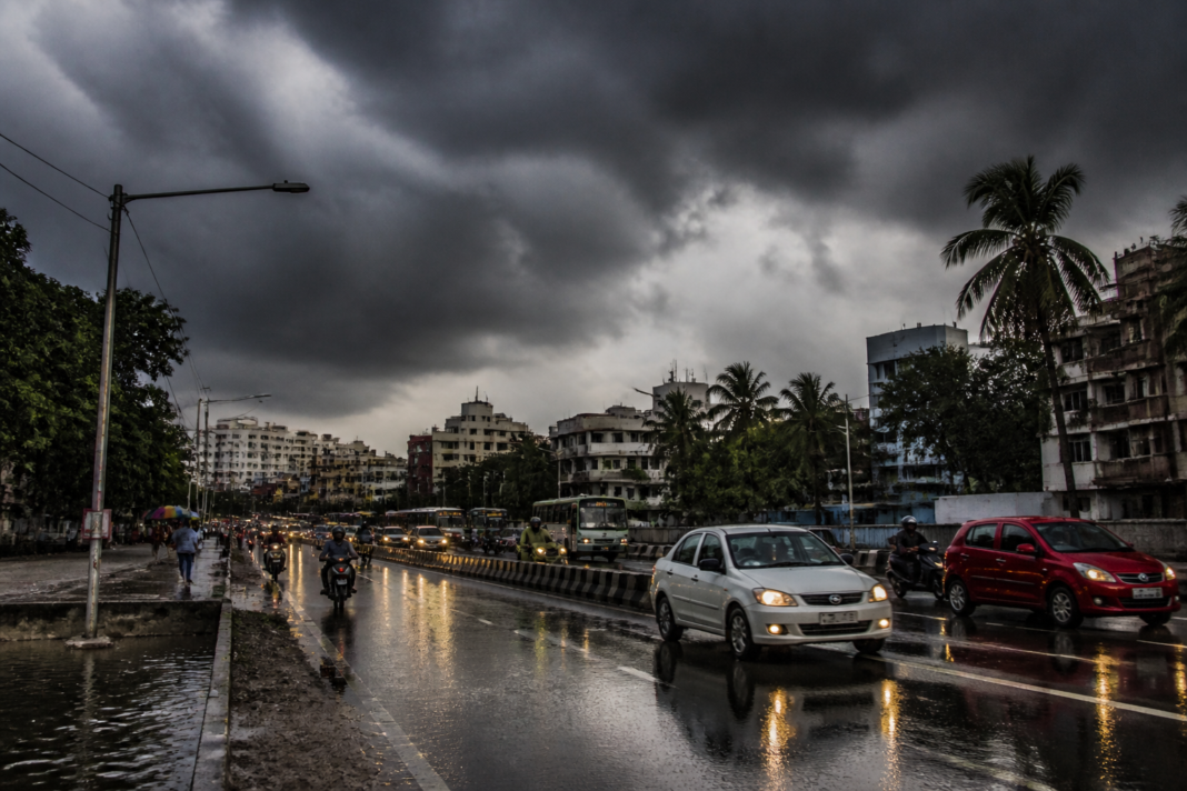 Chennai rain forecast showing storm clouds over a busy urban road with wet traffic conditions.