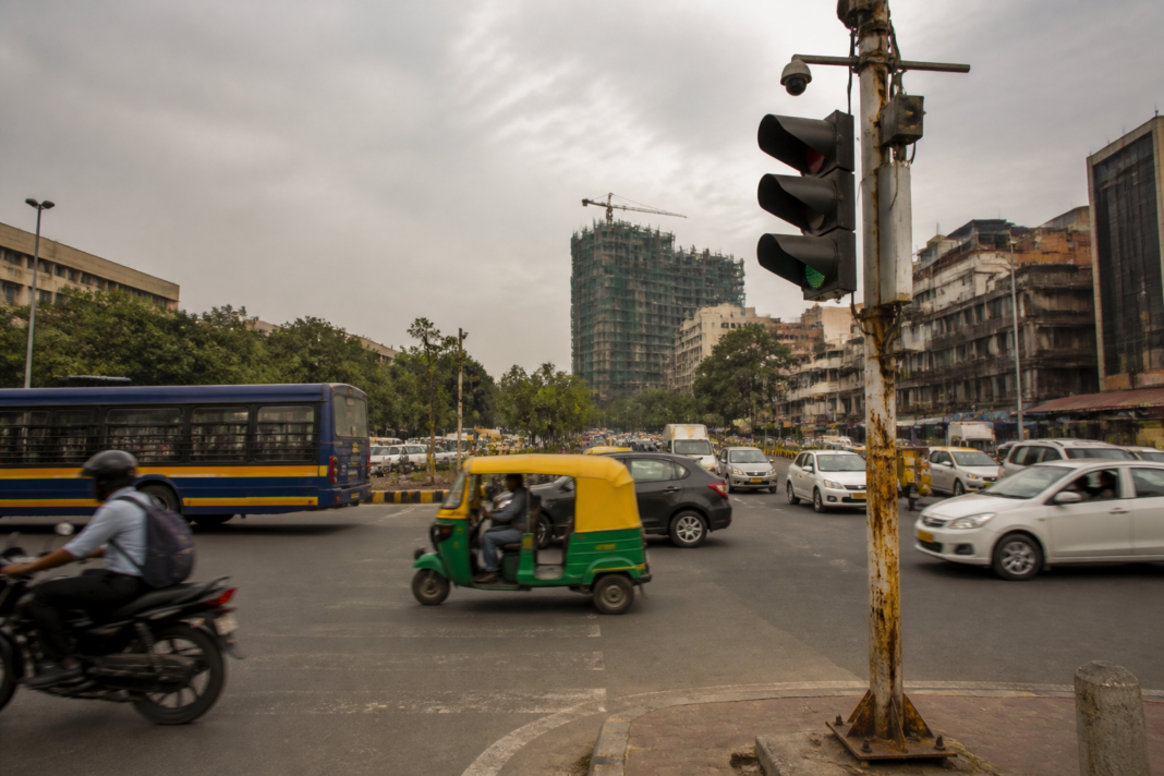 Delhi NCR urban safety concerns shown through a traffic signal pole, busy road and dense buildings