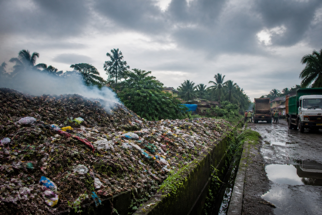 Vasai Pachubandar garbage dump with mixed waste and smoke rising near a residential area