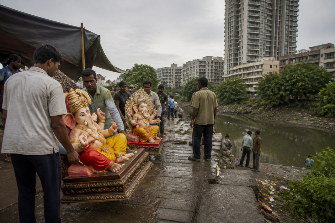 Mira-Bhayandar Ganesh idol immersion site near a creek, with municipal workers handling festival idols.