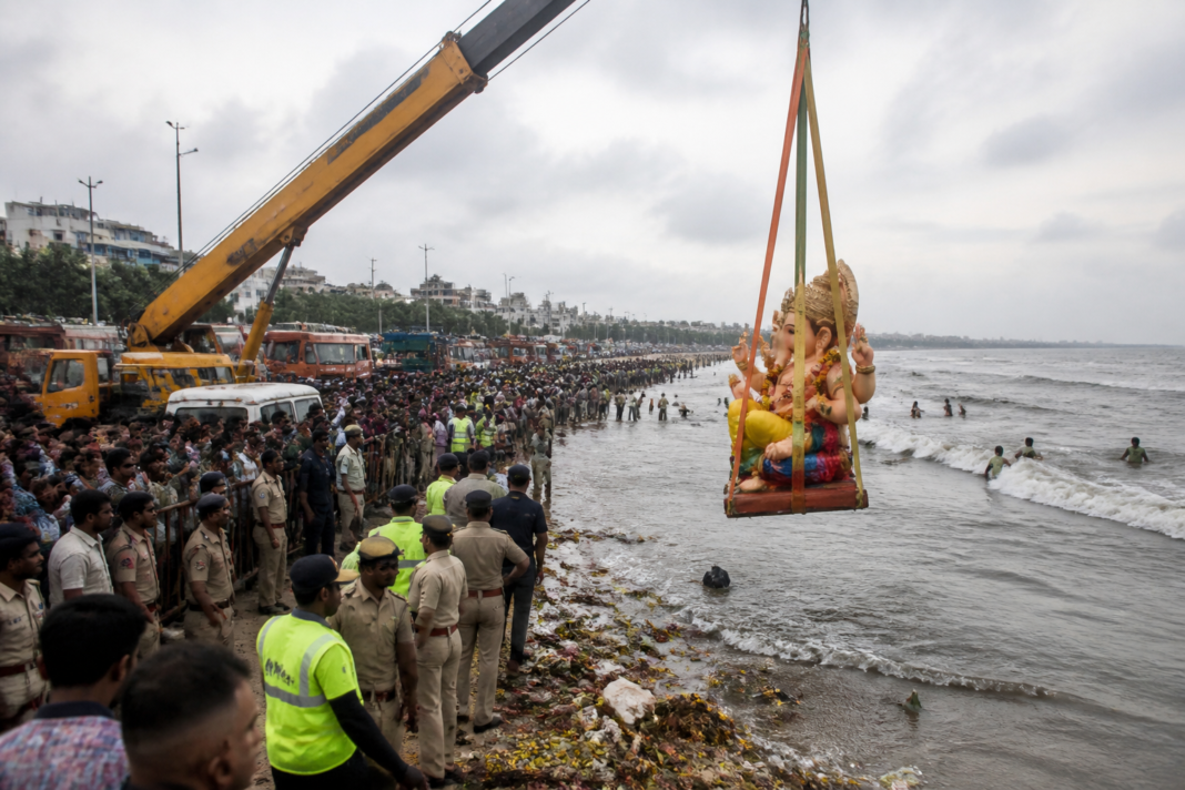 Chennai idol immersion at a beach with cranes, devotees and idol debris near the shoreline