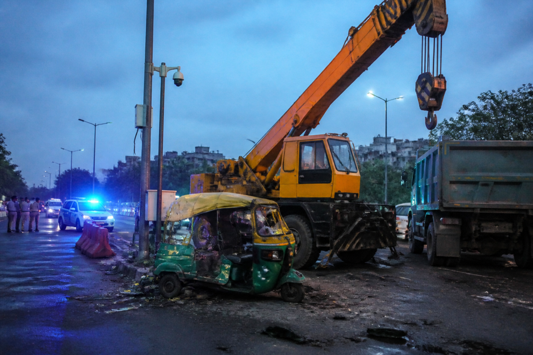 Delhi CCTV installation crash site with a crane and damaged auto-rickshaw on a Sarita Vihar road