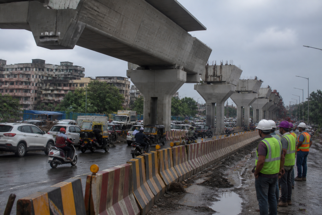 Mumbai Metro 9 construction site near Kashimira with elevated viaduct work beside a busy road
