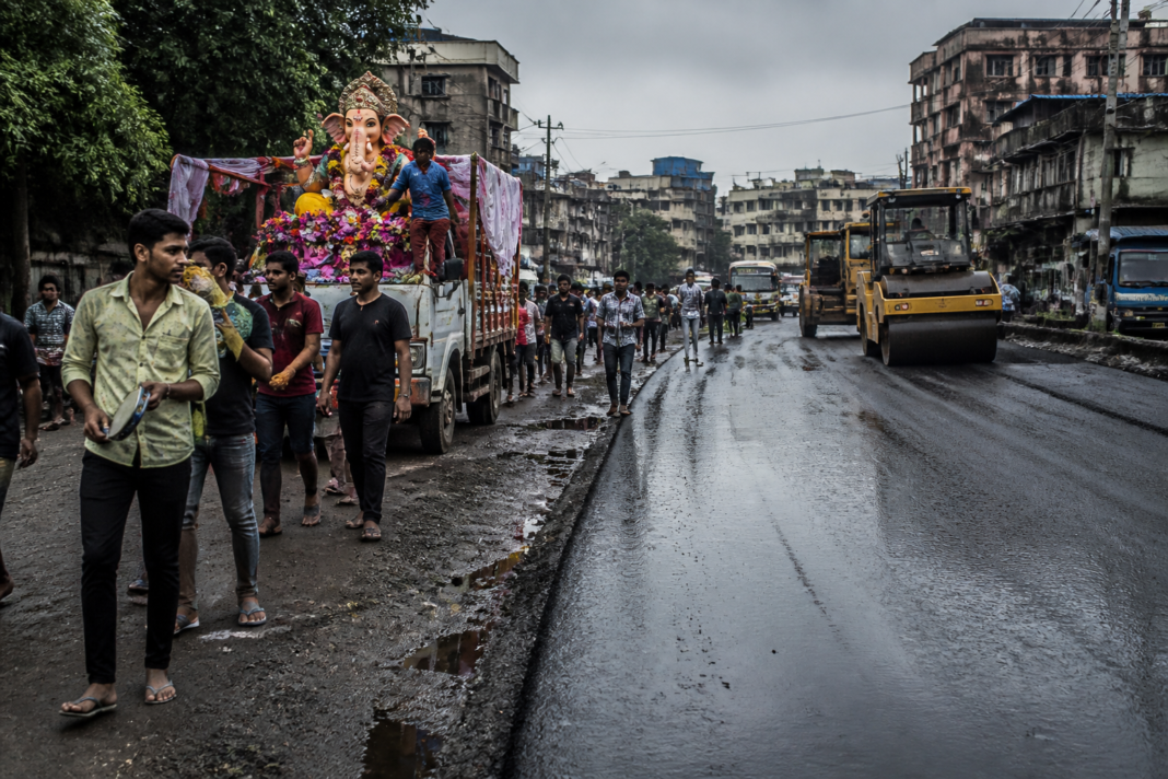 Nalasopara road repairs leave wet asphalt and potholes along a Ganpati immersion route.