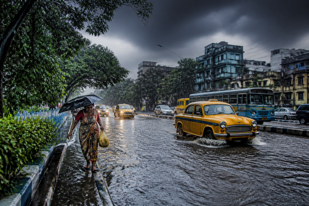 Kolkata rain alert showing dark storm clouds over a waterlogged urban road.