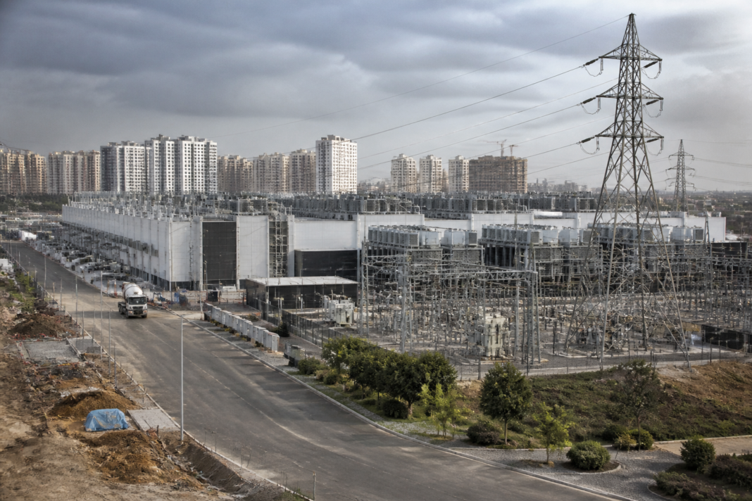 AI data centre investment represented by a large Indian data centre beside power infrastructure.