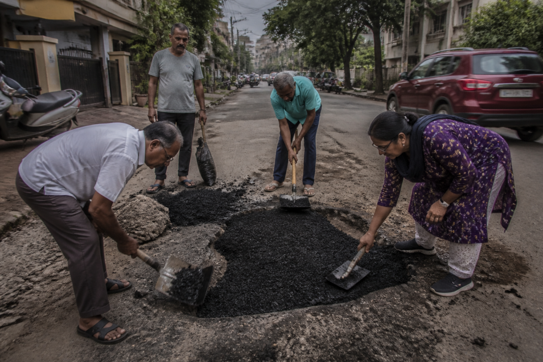 Residents repairing Bengaluru potholes with cold-mix asphalt on a damaged urban road