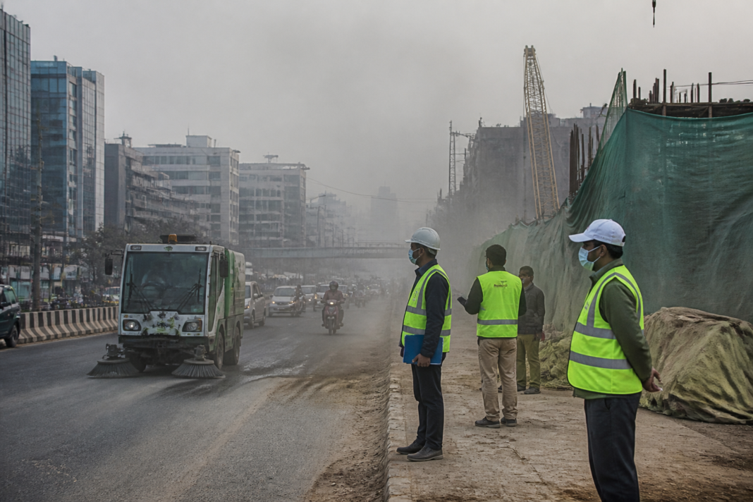 Delhi winter pollution teams monitor a dusty road near construction and traffic.