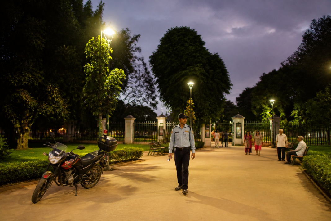 Delhi parks security patrol near a lit park pathway with boundary fencing and trees