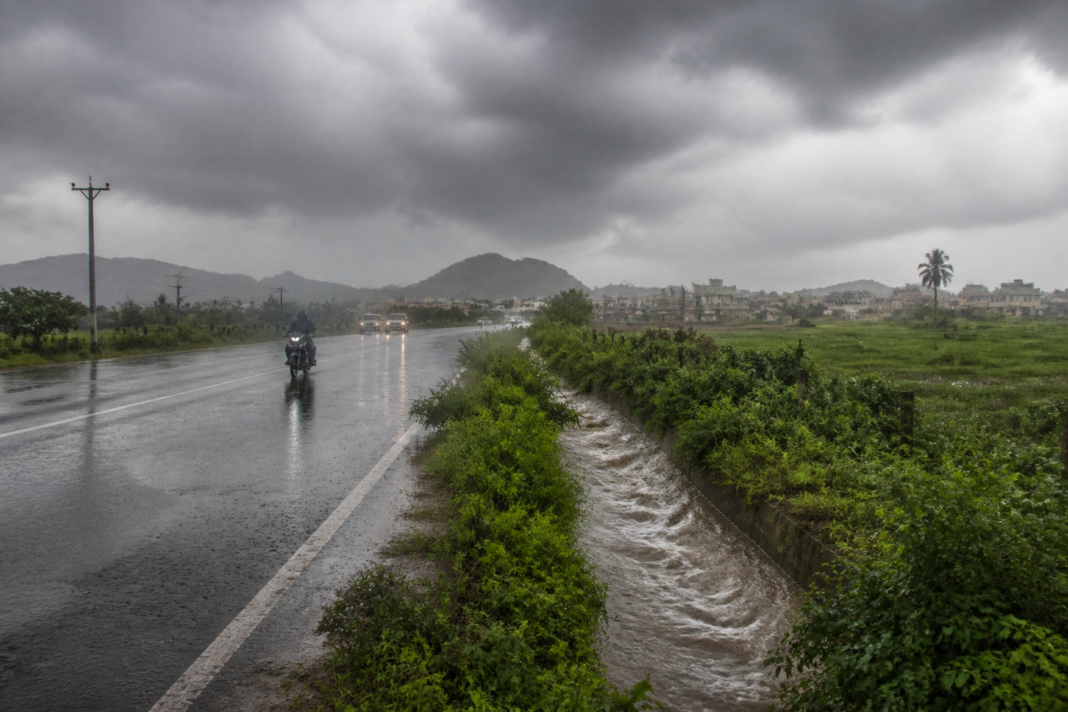 Karnataka rainfall over a rural road near Tumakuru with dark monsoon clouds and wet landscape