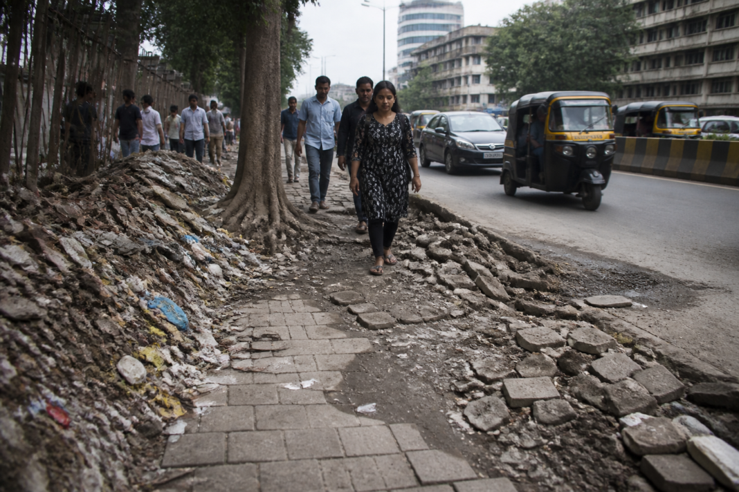 Damaged Thane footpaths obstructed by debris and garbage near a busy urban road