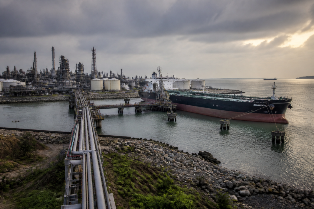 India fuel exports from a coastal refinery with oil storage tanks and tanker loading facilities.