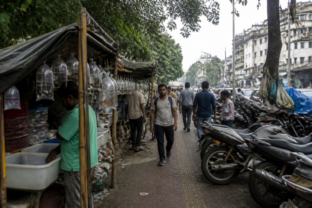 Kolkata footpath encroachment near a busy street market with pedestrians navigating blocked pavement