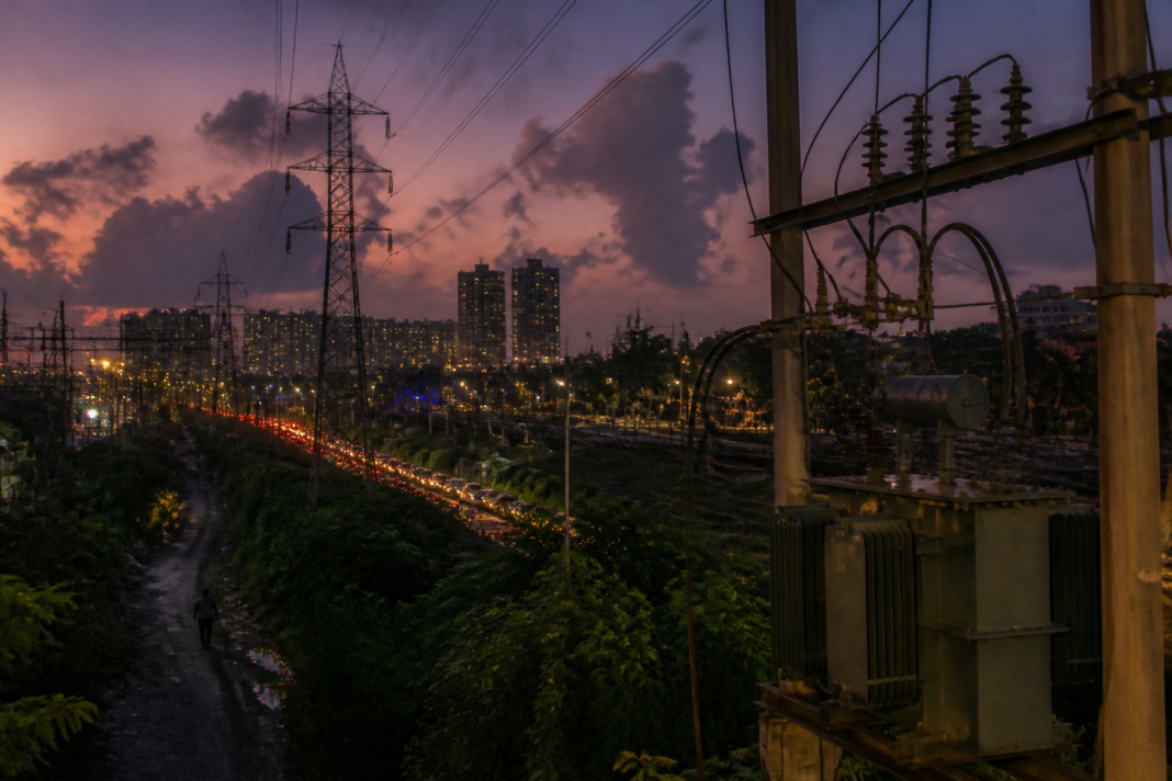 Tamil Nadu power supply infrastructure with electricity transmission lines and urban buildings at dusk